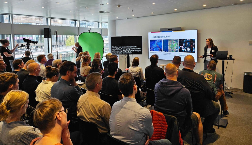 Susanna Laurin from IAAP Nordic presenting on AI-based accessibility testing in front of an attentive audience, as the event is livestreamed with subtitles and sign language interpretation.